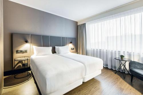 een slaapkamer met een groot wit bed en een raam bij NH Brussels Airport in Diegem