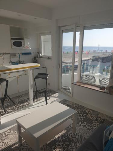 Il comprend un salon avec une table et une cuisine avec des fenêtres. dans l'établissement studio Vue mer au cœur de malo les bains pieds dans l eau, à Dunkerque