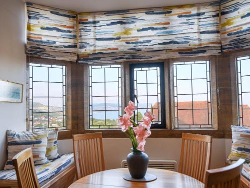 a vase with flowers on a table in a room with windows at 3 Coram Tower in Lyme Regis