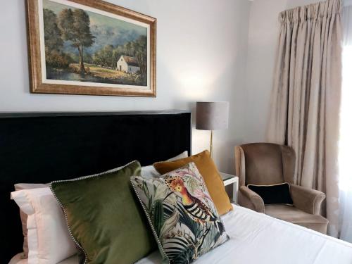 een slaapkamer met een bed en een stoel en een schilderij bij Daisy Place in Franschhoek