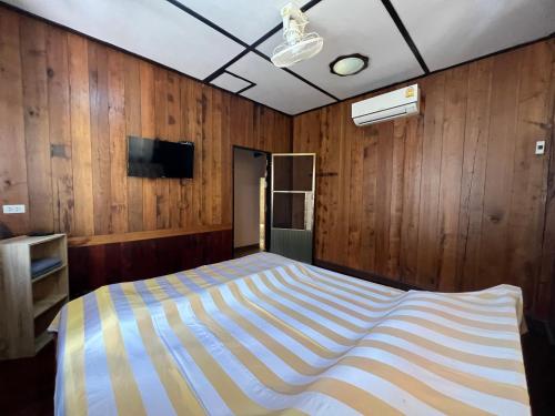 a bed in a room with wooden walls and a tv at ไร่นุชชม รีสอร์ทเขาค้อ in Ban Non Na Yao