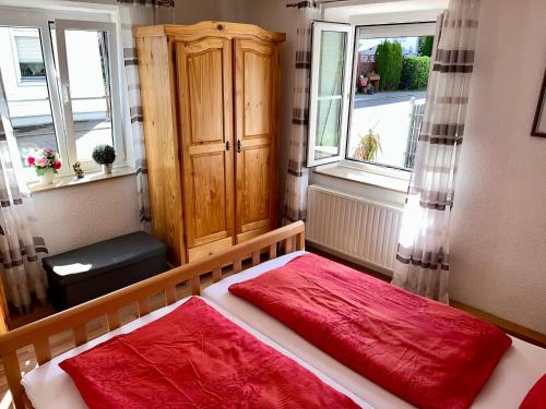 a bedroom with a bed with red sheets and two windows at FeWo HoLiDay ApartMENT Allgäu in Ottobeuren