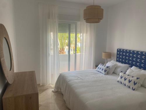een witte slaapkamer met een groot bed met een raam bij Precioso apartamento a pie de playa in Estepona