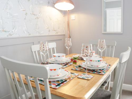 a dining room table with white chairs and a wooden table with glasses at Seaside Retreat in Prestatyn