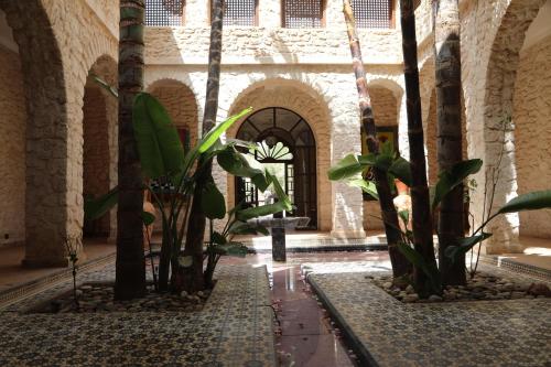 a courtyard with palm trees and a fountain in a building at Jolies chambres d'hôte au Riad Dharma in Essaouira