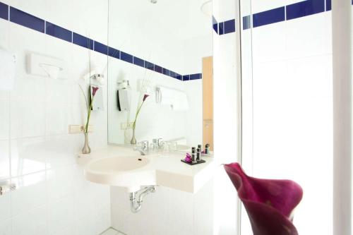 ein weißes Badezimmer mit einem Waschbecken und einem Spiegel in der Unterkunft elaya hotel wolfenbuettel ehemals Rilano 24 7 Hotel Wolfenbüttel in Wolfenbüttel