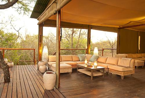 a patio with couches and tables on a wooden deck at Ngama Tented Safari Lodge in Guernsey Nature Reserve