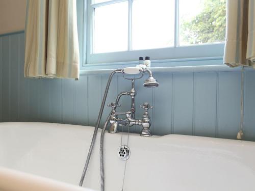 a shower in a bath tub in front of a window at Sawmill Cottage in Royal Tunbridge Wells
