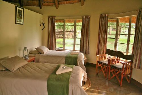 a bedroom with two beds and a chair and windows at Hlane Royal National Park in Simunye