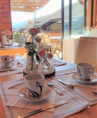 a table with two coffee cups and flowers in a vase at Chalet Hôtel Les Blancs in Pra-Loup