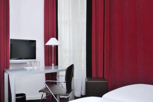 a room with a desk with a television and red curtains at Hôtel Albe Saint Michel in Paris