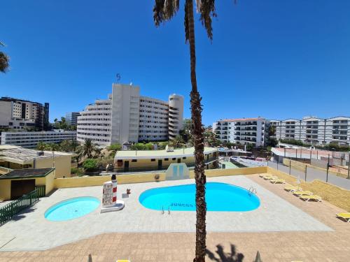 a large swimming pool with palm trees and buildings at The SunSpot Apartment Playa del Inglés in Maspalomas