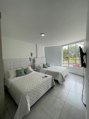 a white bedroom with two beds and a window at Ingenio Park 83 - Apartahotel in Cali