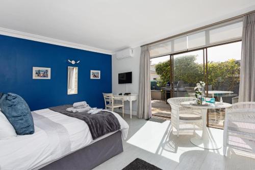 Schlafzimmer mit blauen Wänden, einem Bett und einem Tisch in der Unterkunft OCEAN BREEZE SUNSET BEACH - Cape Town in Kapstadt
