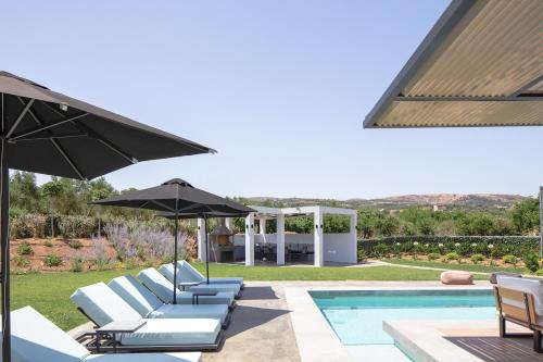a group of chairs and an umbrella next to a pool at Physis Villas - Metal & Wood in Pigi