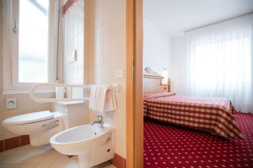 a bathroom with a toilet a sink and a bed at Hotel Daniela in Levico Terme