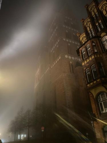a tall building on a foggy street next to a building at The Layhead B&B in Lübeck