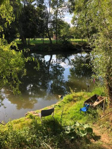 ein Fluss mit zwei Stühlen im Gras daneben. in der Unterkunft Tiny house détente nature la maison du pêcheur in Pulligny