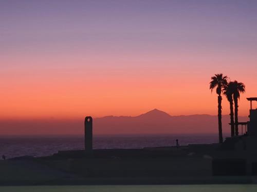 puesta de sol en la playa con palmeras y montañas en Vista Faro Sardina, en Las Palmas de Gran Canaria