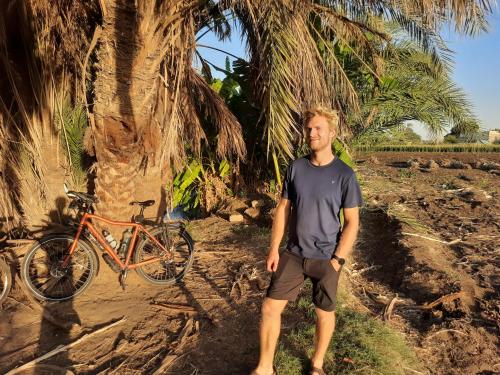 a man standing next to a bike next to a palm tree at Village Room in the Countryside in Minya