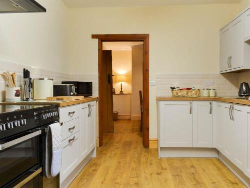 uma cozinha com armários brancos e piso em madeira em Bwthyn Ty Mawr em Llandwrog