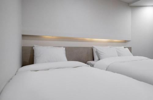 two beds in a room with white sheets and pillows at Geoje Mongdol Beach H Avenue Hotel in Geoje 