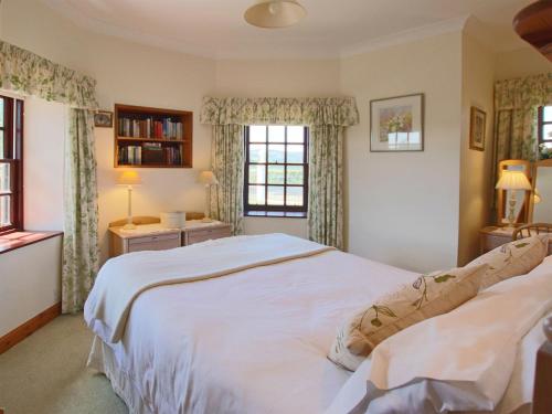 a bedroom with a large white bed and two windows at Conheath Gatelodge Cottage in Kingholm Quay