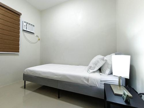 a white room with a bed and a table with a lamp at Manzil Anilao B&B in Mabini
