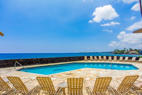 a pool with chairs and the ocean in the background at The Sea Village #1302 in Kailua-Kona
