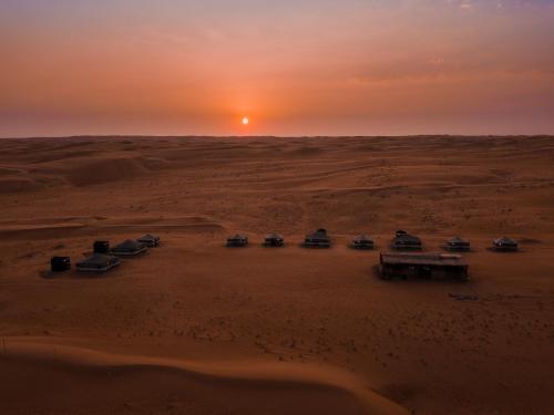 Sands Dream Tourism Camp في شاحك: مجموعة سيارات تقف في الصحراء وقت الغروب