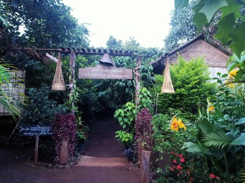 an entrance to a garden with a sign and flowers at Tribal Village Homestay & Trekking in Banlung