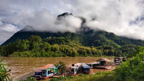 a bunch of boats parked on a river with a mountain at Arthith Guesthouse in Nongkhiaw
