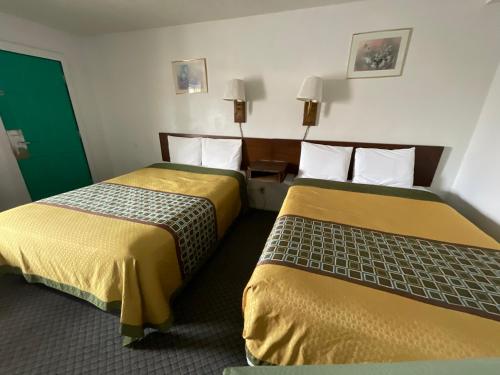 two beds in a hotel room with yellow and green sheets at Kansan Motel in Liberal
