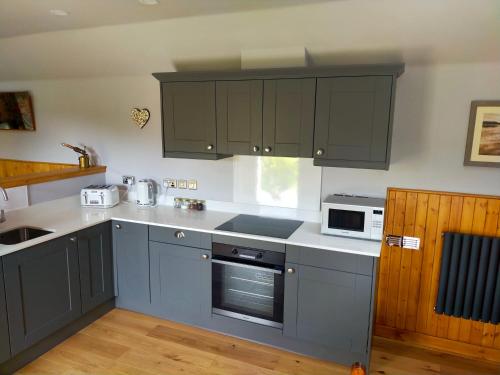 eine Küche mit grauen Schränken und einer Mikrowelle in der Unterkunft Braeside Cottage - Adorable 2 Bedroom Eco-Friendly Character Cottage in Pitlochry