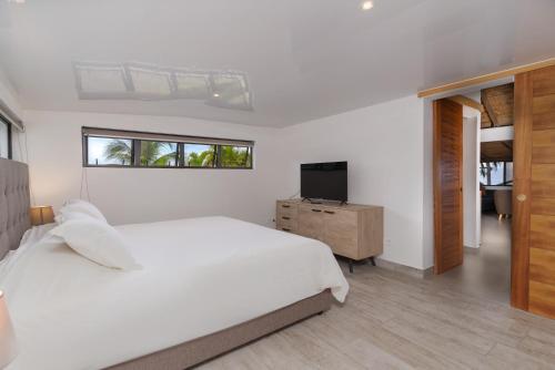 een witte slaapkamer met een bed en een televisie bij Jolie Maison Vue Ocean et Moorea in Punaauia