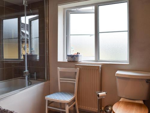 a bathroom with a toilet and a chair and a window at Cosy Cottage in Bourton on the Hill