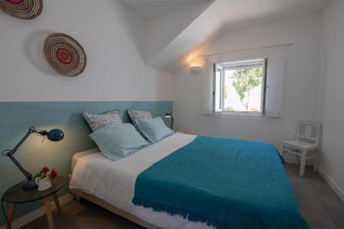 a bedroom with a bed with a blue blanket and a window at Casa no Rio - River House in Vila Nova de Milfontes