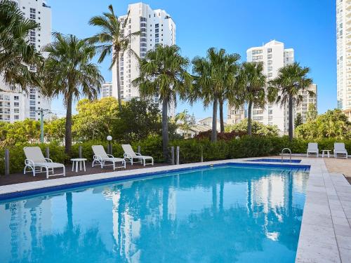 a swimming pool with chairs and palm trees and buildings at Maldives Resort Main Beach, Gold Coast in Gold Coast