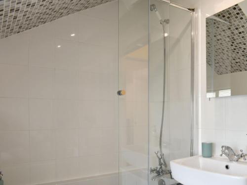 a white bathroom with a shower and a sink at Cenwulf Cottage in Winchcombe