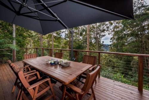 a wooden table and chairs on a deck with an umbrella at Hope Cottage - Tamborine Mountain in Mount Tamborine