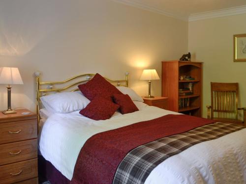 1 dormitorio con 1 cama grande con almohadas rojas en Belstane Cottage en Straiton