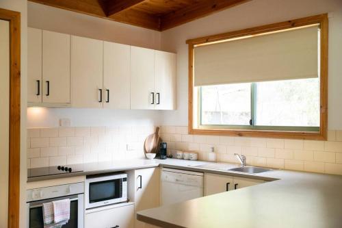 a kitchen with white cabinets and a sink and a window at Country Lane Cottage in Halls Gap