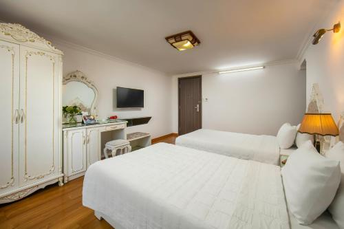 a white bedroom with two beds and a mirror at Hanoi Kingly Hotel in Hanoi