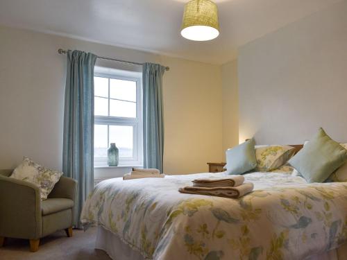 a bedroom with a bed and a chair and a window at Slaters Cottage in Middleham