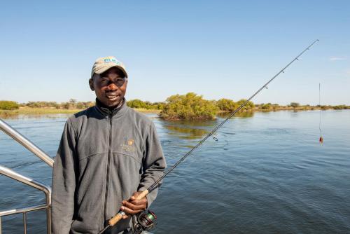 a man standing on a boat holding a fishing rod at Zambezi Mubala Camp in Katima Mulilo