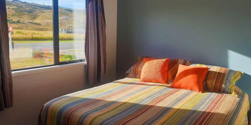 a bed with orange pillows in a room with a window at Rough Ridge Cottage ~ your haven in Central Otago in Oturehua