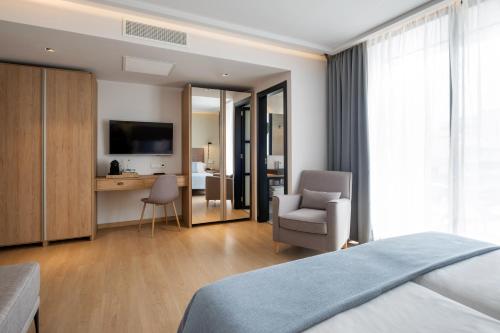 a bedroom with a bed and a chair and a television at Kyrat Amarac Suites in Cala Millor