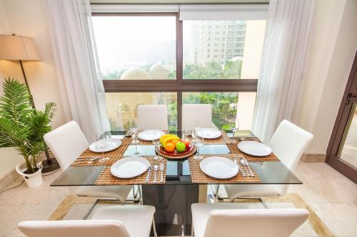ein Esszimmer mit einem Glastisch und weißen Stühlen in der Unterkunft Bespoke Holiday Homes - Palm Jumeirah- 2 Bedroom with Gym, Beach & Pool Access, Fairmont South in Dubai