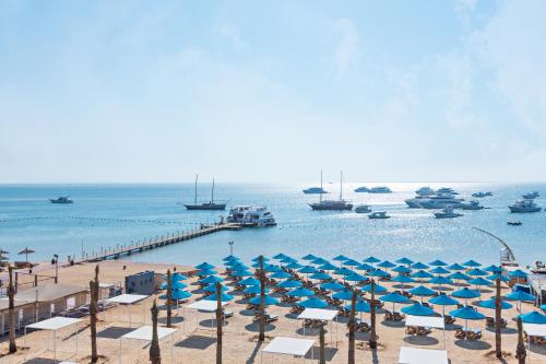 a beach with blue umbrellas and boats in the water at Pickalbatros Blu Spa Resort - Adults Friendly 16 Years Plus- Ultra All-Inclusive in Hurghada