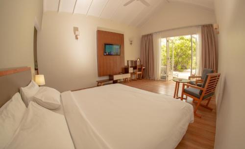a bedroom with a white bed and a table and chairs at Hondaafushi Island Resort in Vaikaradhoo